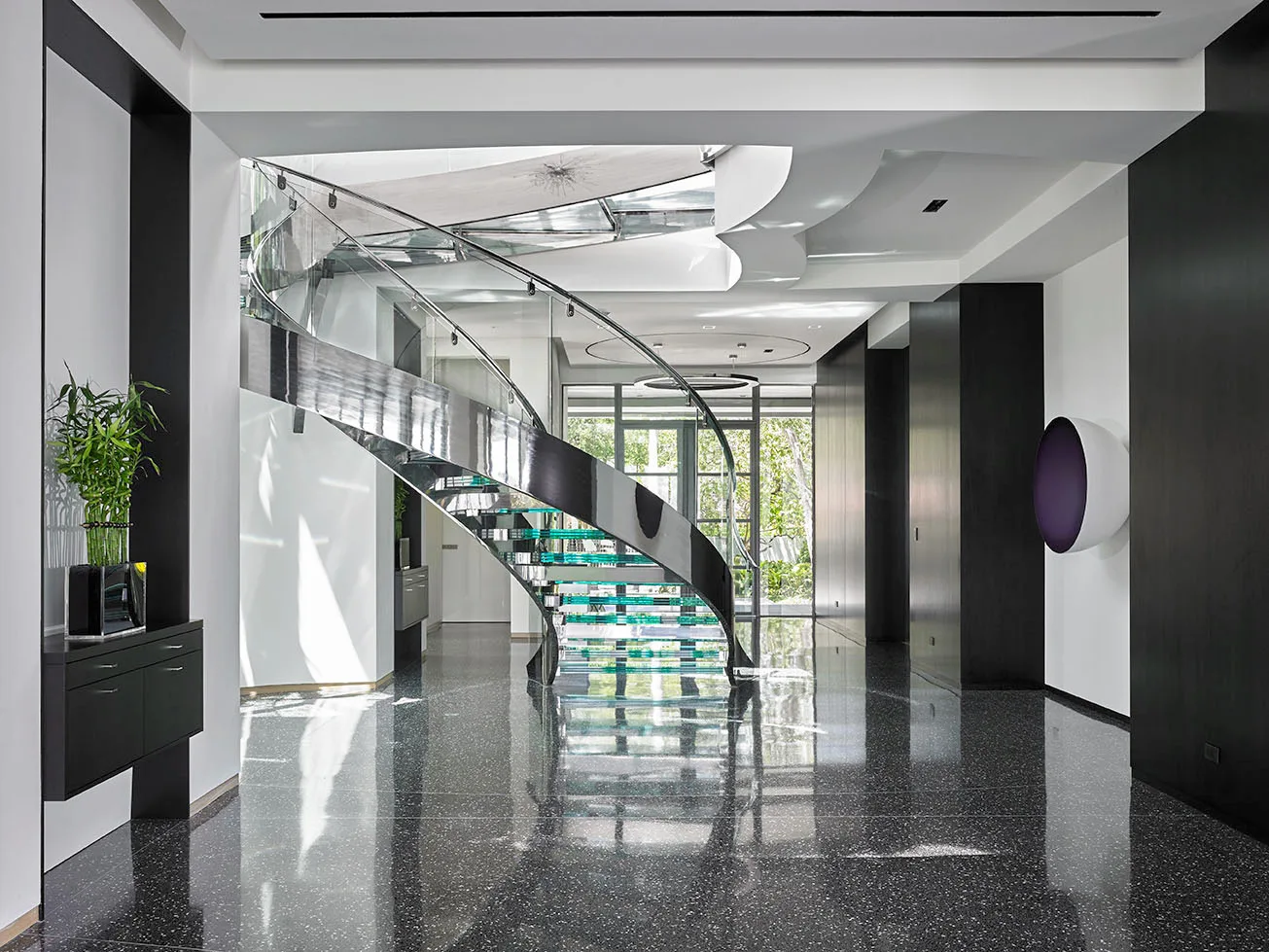 Contemporary Boca Raton villa foyer with a curved glass staircase over a terrazzo floor