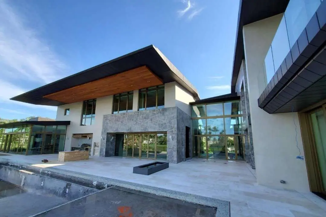 Wide view of the villa facade combining honed grey stone and glazing under a low roofline