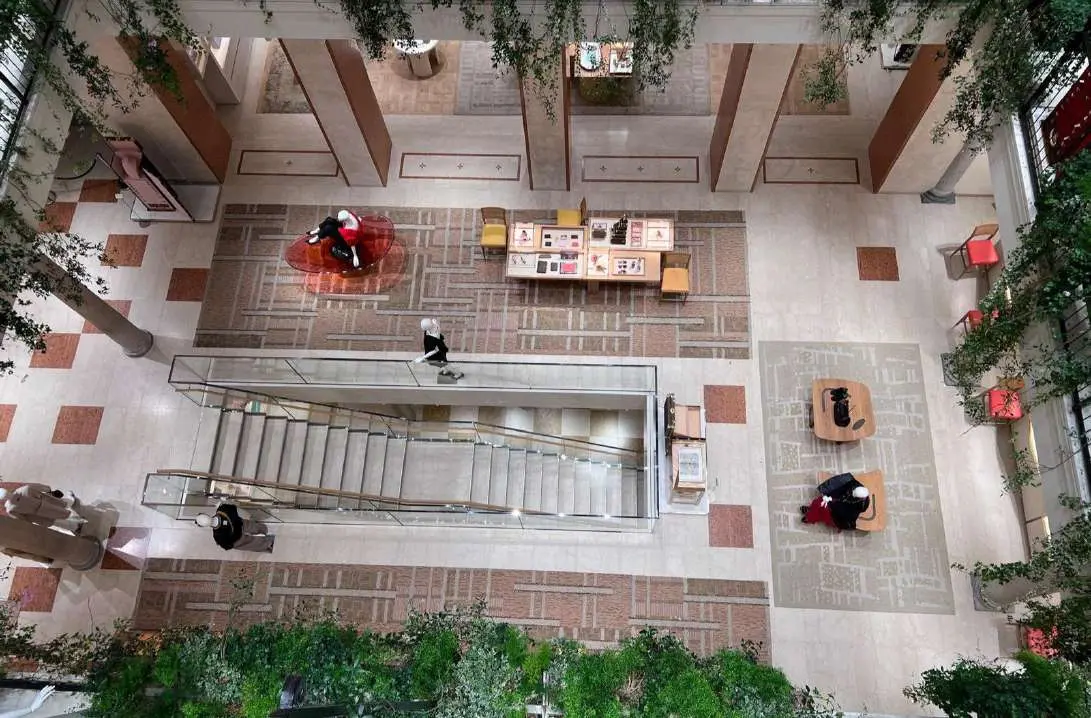 Multi-level atrium under a glass roof with greenery and railings