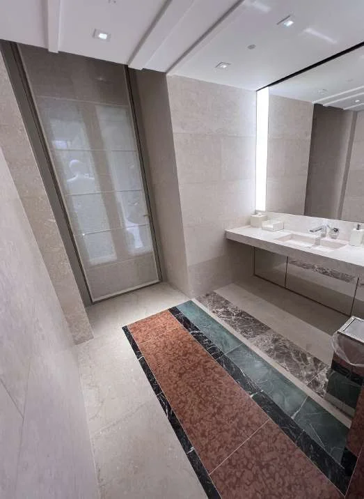 Powder room clad in marble with a decorative floor band at the vanity
