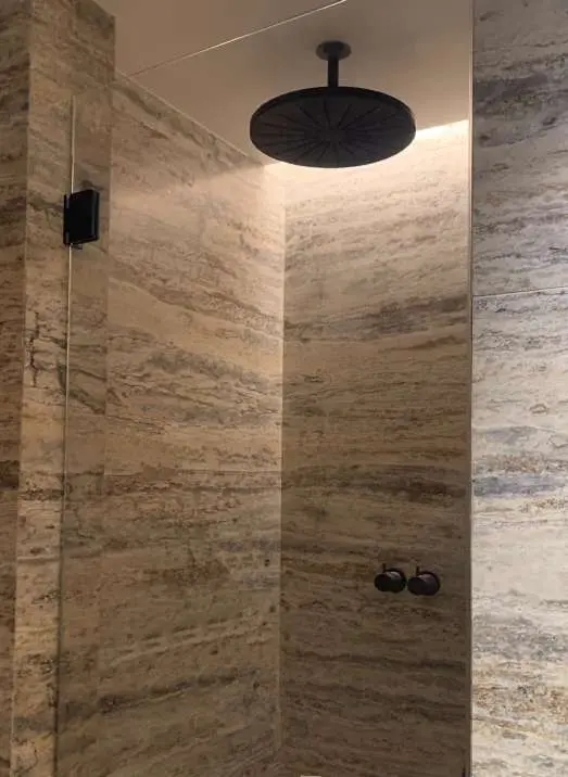 Travertine shower with a black ceiling rain head