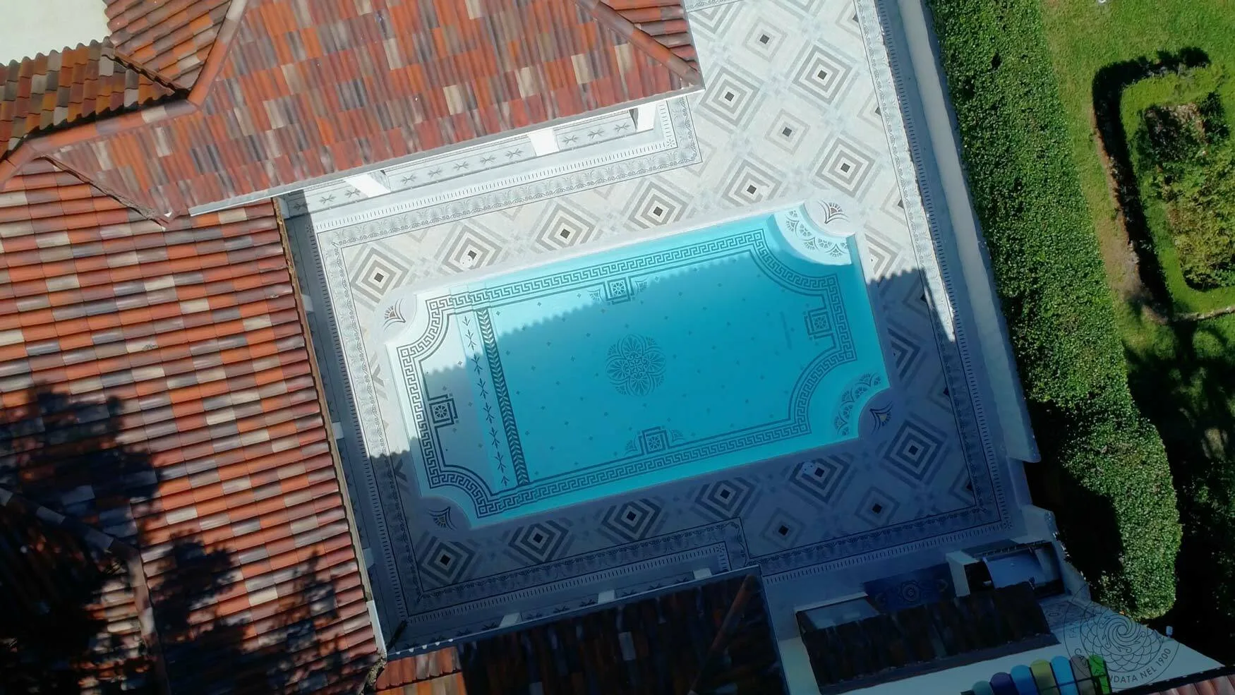 Aerial view of a mosaic swimming pool with a Greek-key border set into a patterned terrace in Sarasota