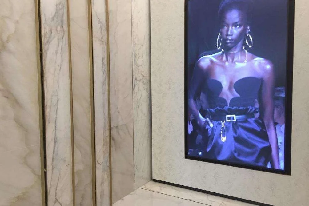 Marble-clad gallery wall with a framed Versace campaign image and benches
